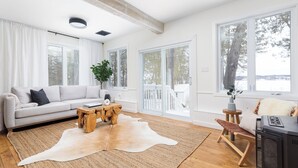 A modern living room with a sofa, coffee table, and a large rug. - The Hudson Guest House | Waterfront with Hot Tub (Prince Edward)