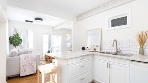 A modern kitchen with white cabinetry, a built-in sink, and a wooden dining table. - The Hudson Guest House | Waterfront with Hot Tub (Prince Edward)