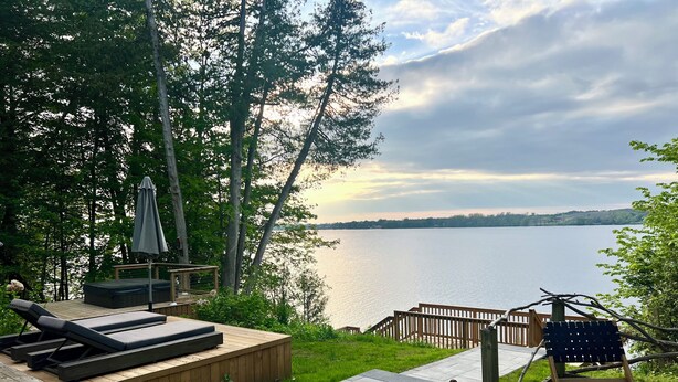A wooden deck with lounge chairs and a hot tub overlooking a lake. - The Hudson Guest House | Waterfront with Hot Tub (Prince Edward)