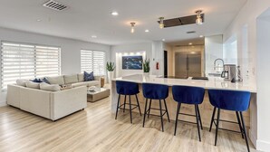 A modern kitchen with a central island, bar stools, and a dining area. - SoFloasis - Home w/ Heated Pool, close to beaches (Lighthouse Point)