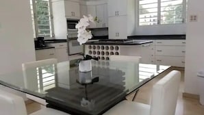 A modern kitchen with white cabinets, a glass dining table, and white chairs. - Urban Paradise (San Juan)