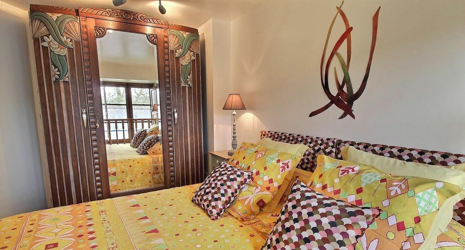 A room with a bed, a mirror, a lamp, and a wall decoration.