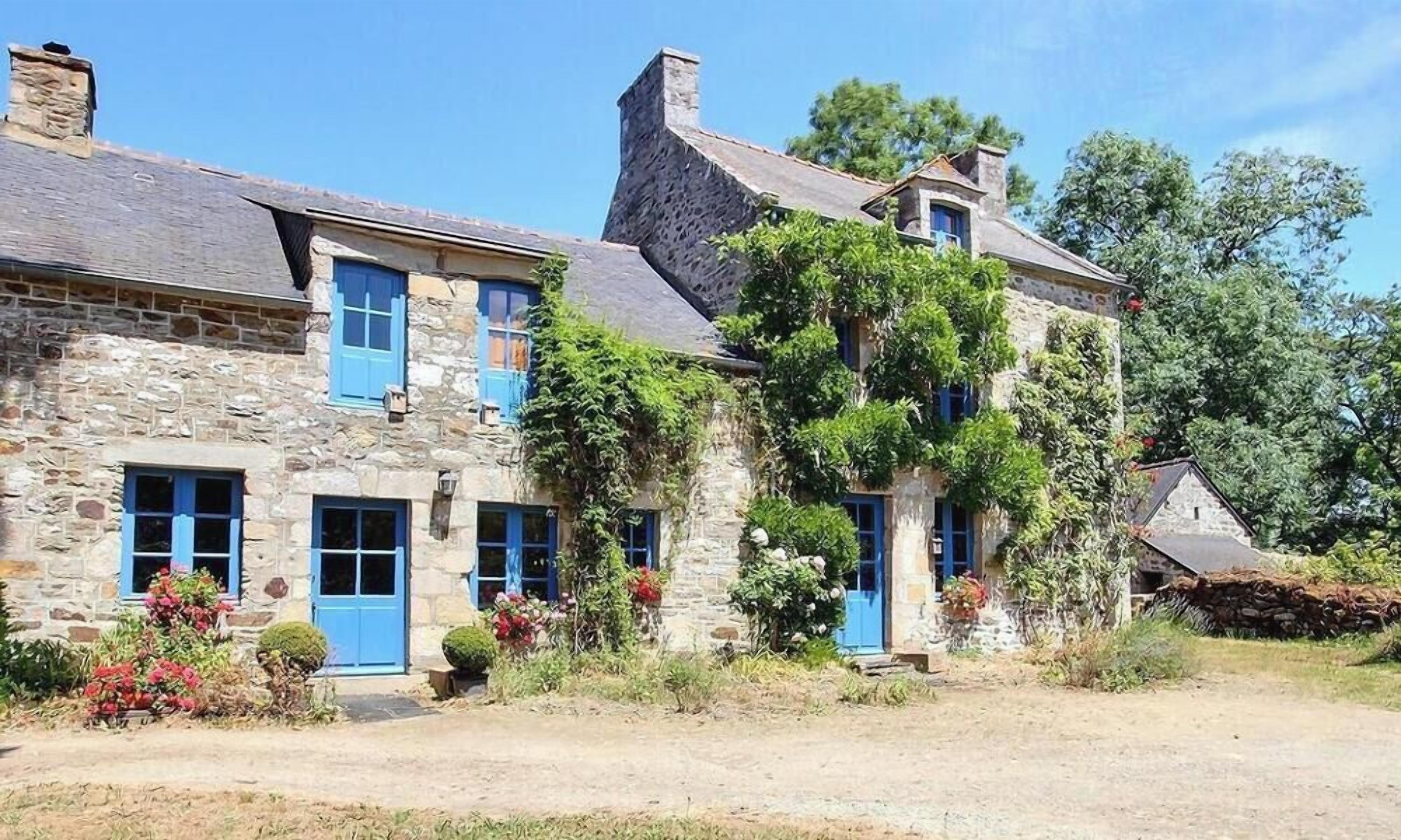 A stone building with multiple doors and windows, surrounded by greenery and trees.