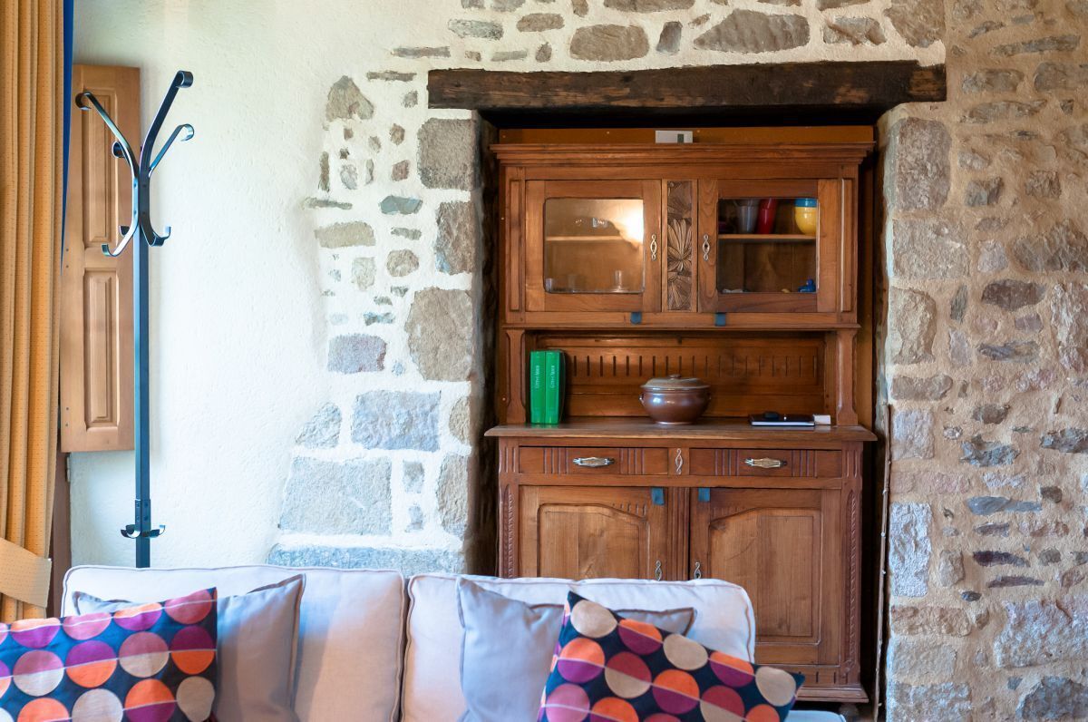 Una stanza accogliente con parete in pietra, mobiletto in legno con vetri e divano imbottito con cuscini decorati.