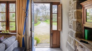Een rustieke kamer met een stenen muur, een houten deur naar buiten, een bank en een klein tafeltje met kaarsen.