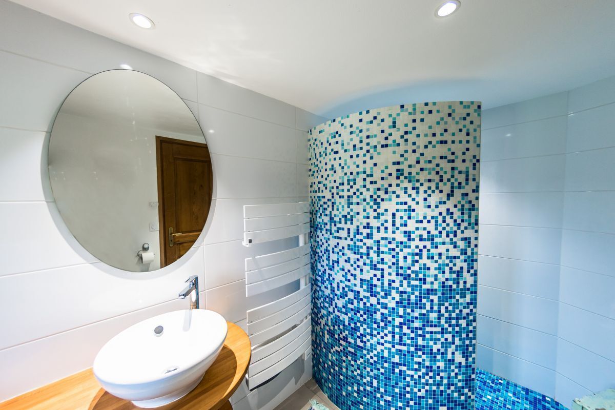 Une salle de bain avec un miroir rond, un lavabo blanc et un mur recouvert de mosaïques.