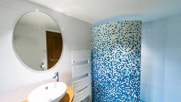 Une salle de bain avec un miroir rond, un lavabo blanc et un mur recouvert de mosaïques.