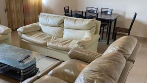 Un salon avec un canapé beige, une table basse en verre et une table à manger avec des chaises.