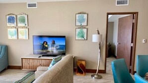 Een woonkamer met een televisie, een bank, een stoel en kunstwerken aan de wanden.
