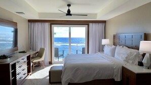 Een hotelkamer met een bed, bureau, stoel, televisie en uitzicht op de oceaan.