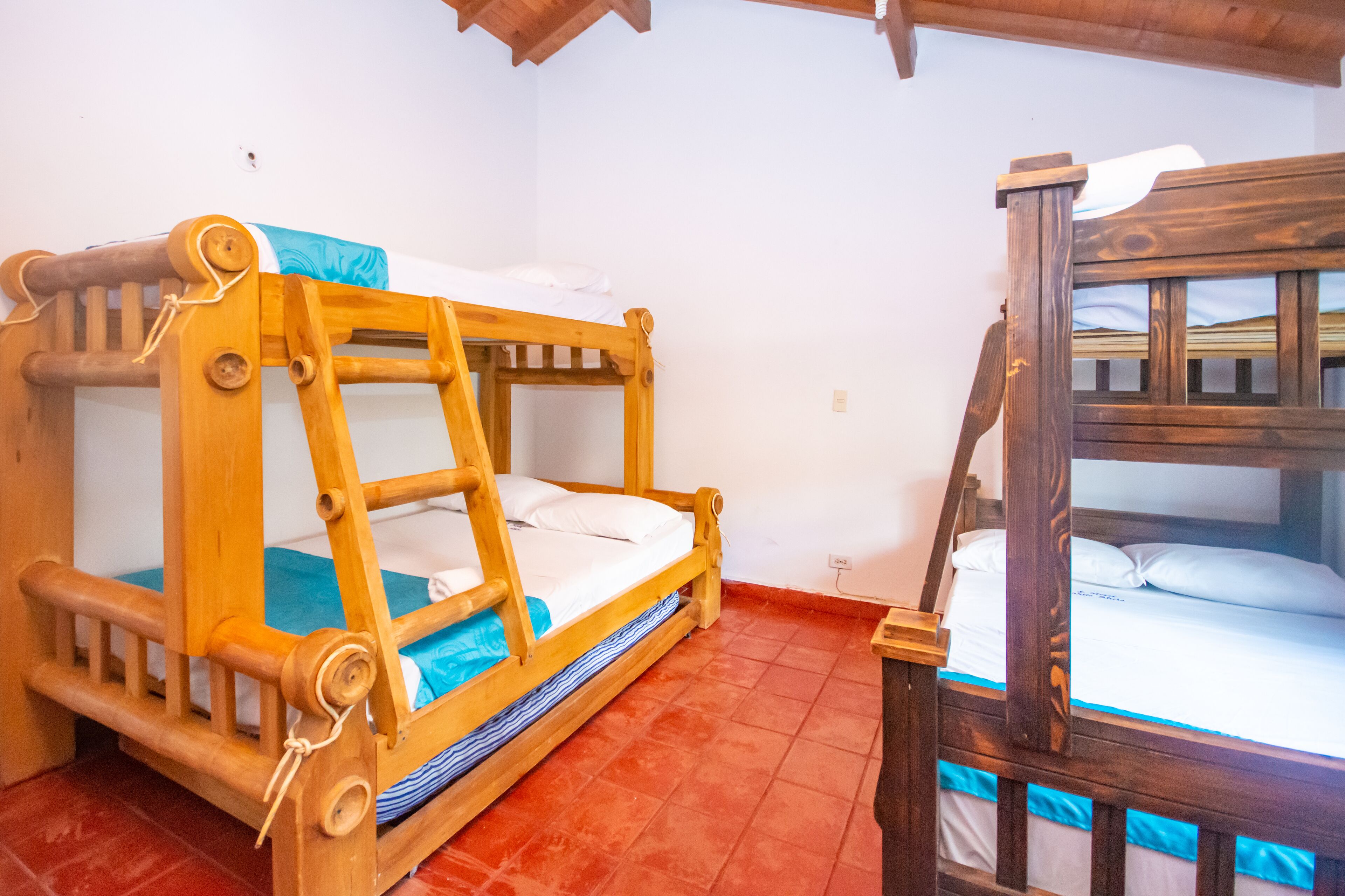 A wooden bunk bed with a blue blanket and white pillows, a wooden ladder, and a red-tiled floor.