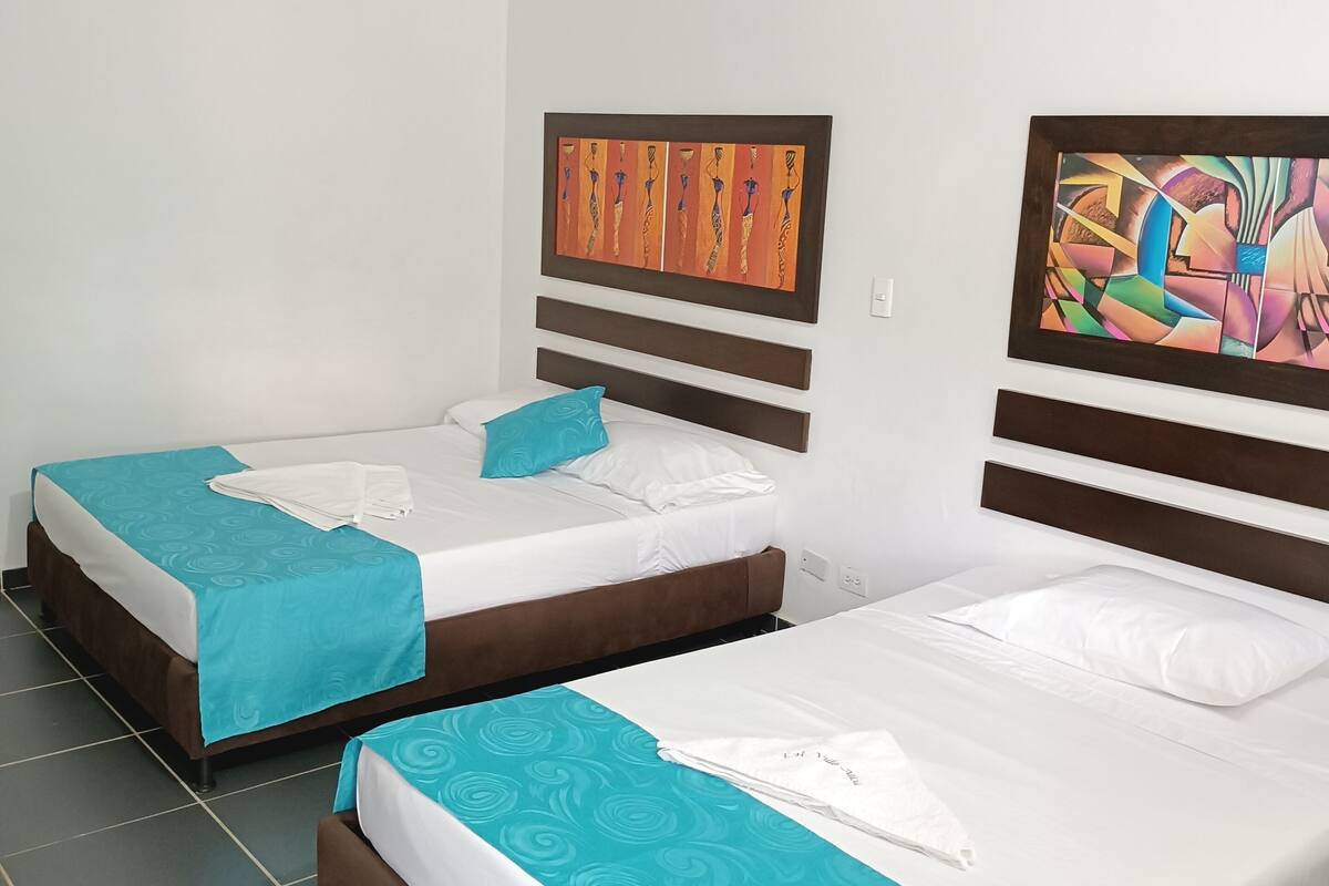 Two single beds with teal bedding, a wooden headboard, and a colorful abstract painting on the wall.