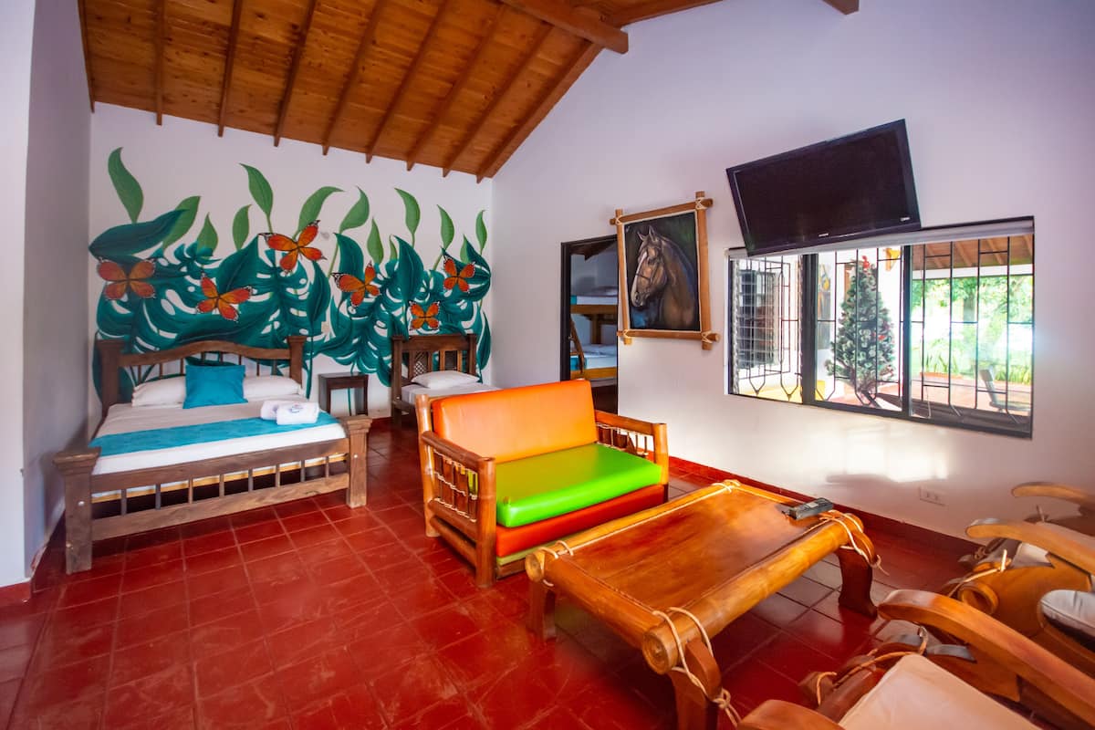 A room with a bed, a wooden bench, a table, and a TV mounted on the wall.