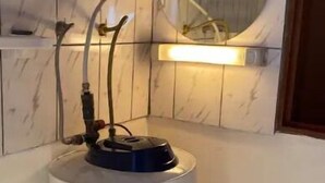 Un chauffe-eau doté de tuyaux et d’un panneau de commande, fixé sur un mur recouvert de carreaux.