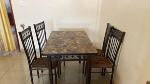 Une table à manger avec quatre chaises, un sol carrelé et un mur uni.