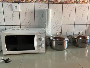 Une cuisine avec un four à micro-ondes blanc, deux casseroles en acier inoxydable et une prise électrique sur le mur.