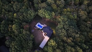 An aerial view of a property surrounded by dense forest, featuring a swimming pool, a covered patio, and a well-maintained lawn. - Fall Retreat | Hot Tub, Games & Wine Country (South Haven)