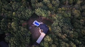 Luchtbeeld van een pand, omringd door dicht bos, met een zwembad, een overdekt terras en een verzorgd gazon.