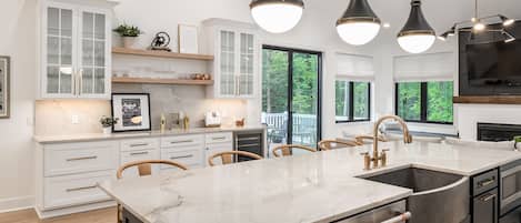 A modern kitchen with white cabinetry, a marble countertop, and pendant lighting.