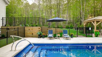 A backyard with a swimming pool, a wooden deck, and a fenced area with chairs and umbrellas.