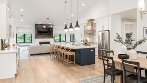 Een moderne keuken met een groot kookeiland, hanglampen en een eethoek met tafel en stoelen.