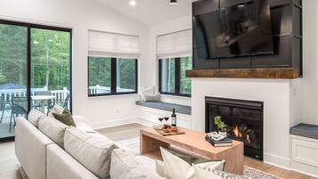 A modern living room with a sofa, coffee table, fireplace, TV, and large windows.