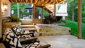 Een terras buiten met houten meubels, een vuurkorf en uitzicht op de achtertuin.