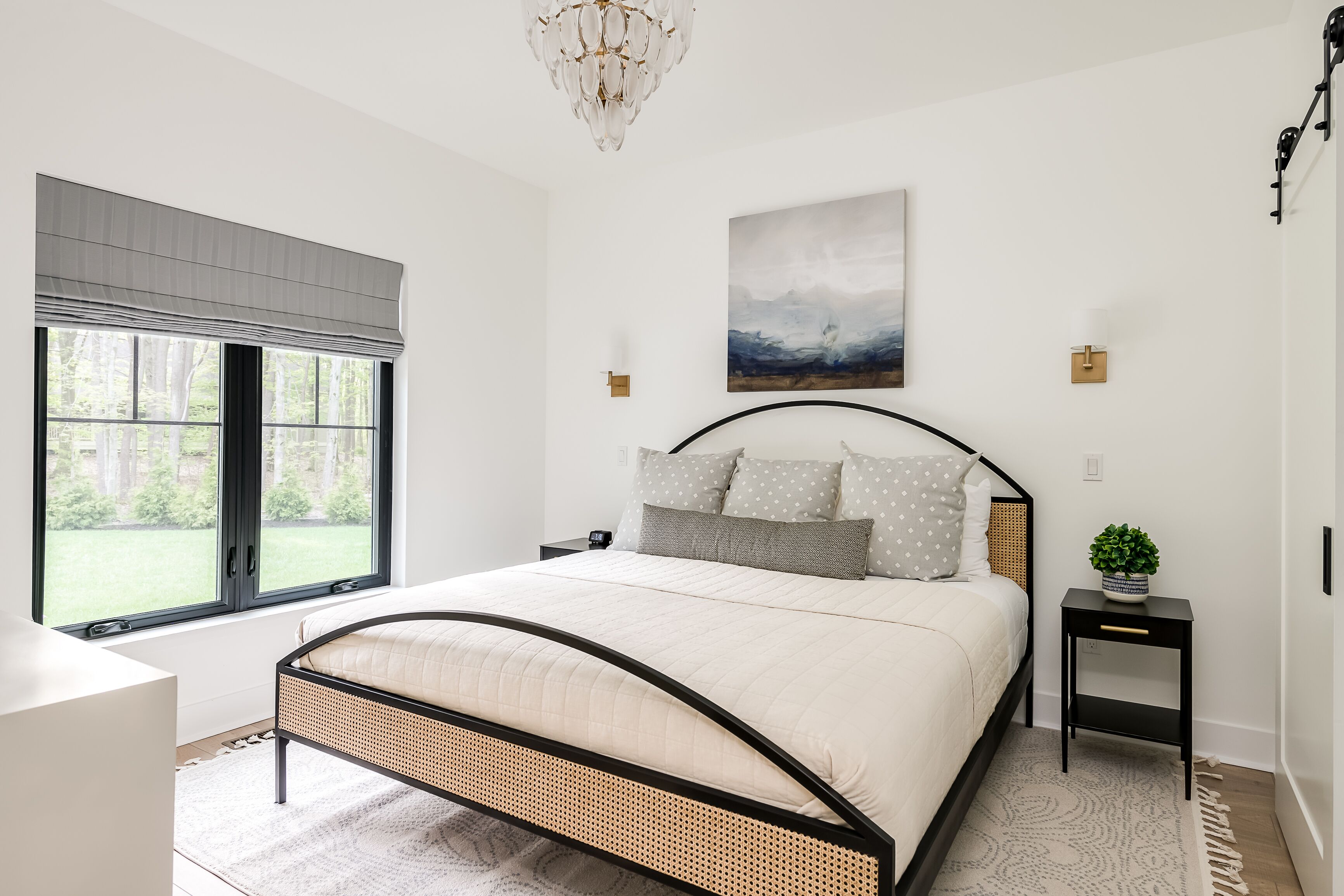 A bedroom with a bed, a window, a chandelier, and a painting on the wall.