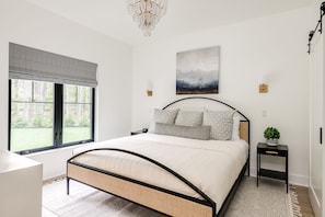 Een slaapkamer met een bed, een raam, een kroonluchter en een schilderij aan de muur.