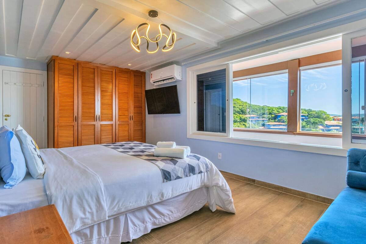 A bedroom with a bed, wooden wardrobe, TV, air conditioning unit, and a window with a view.