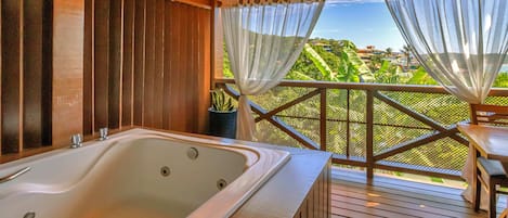 Een houten terras met een jacuzzi, uitzicht op groen en een overdekt gebied met gordijnen.