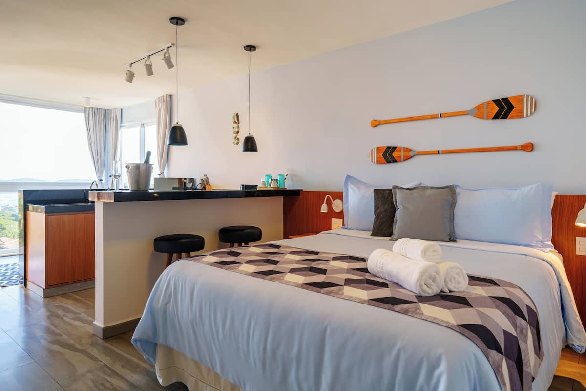 A modern hotel room with a large bed, a small kitchenette, and a view of the outdoors.