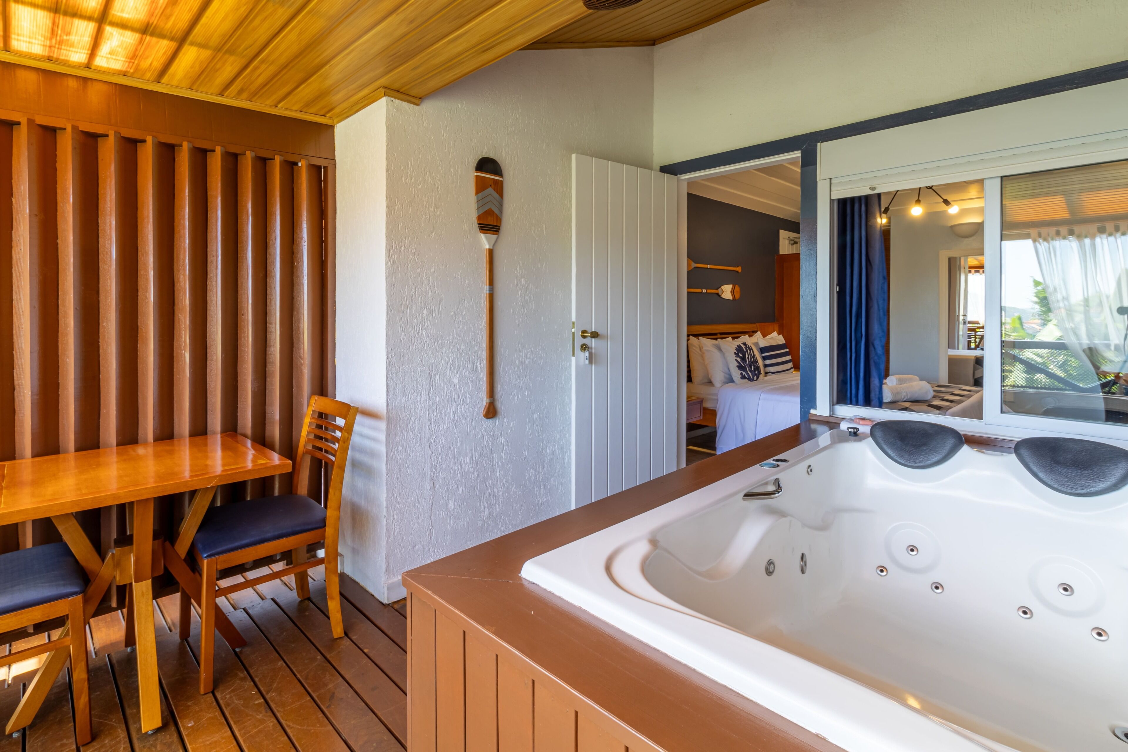 A wooden deck with a hot tub, a table with chairs, and a door leading to a room.