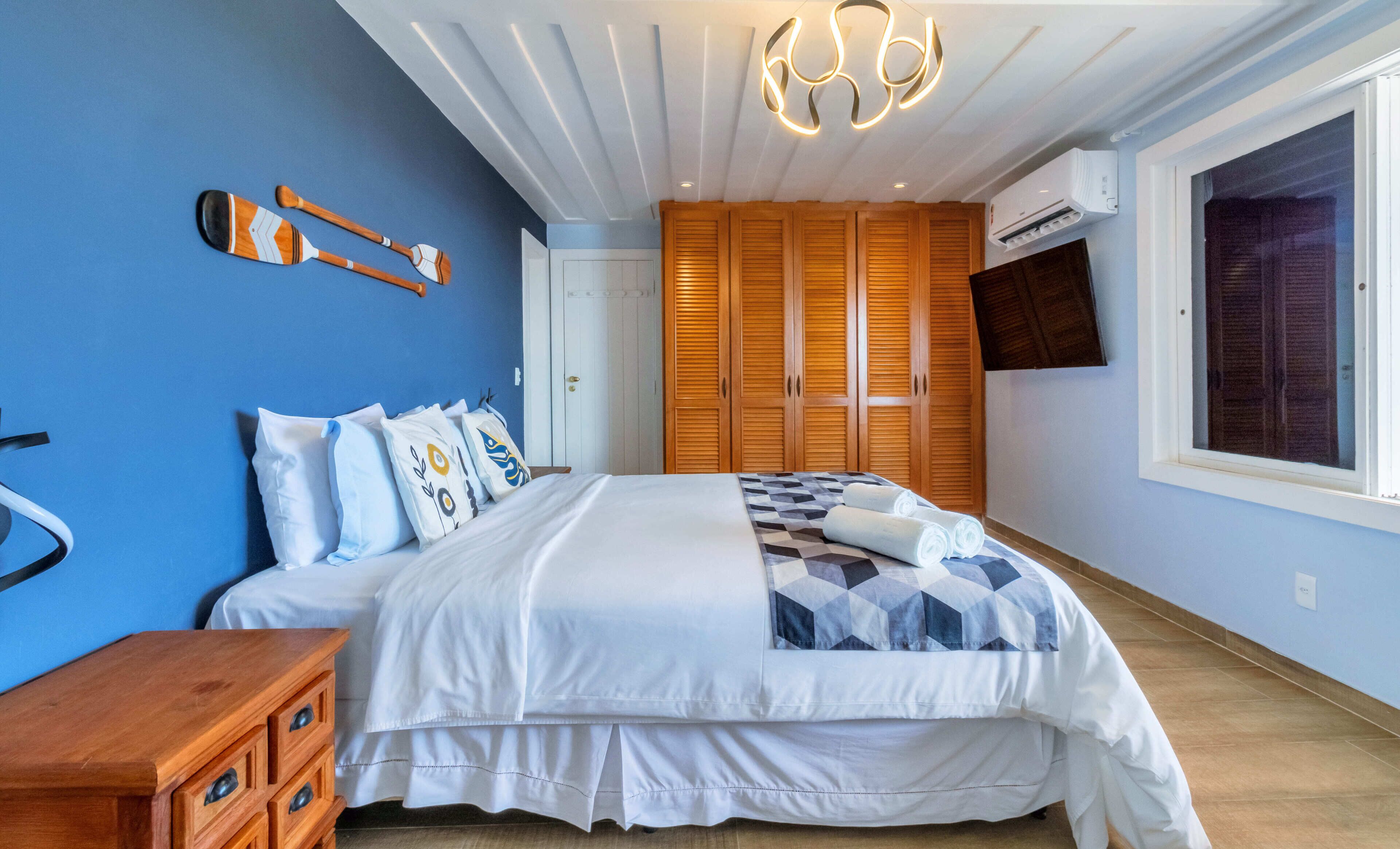 A bedroom with a bed, wooden wardrobe, and a TV on the wall.