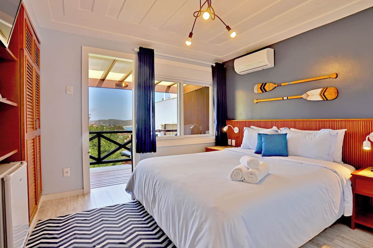 A hotel room with a large bed, a balcony with a view, wooden furniture, and a ceiling light fixture.