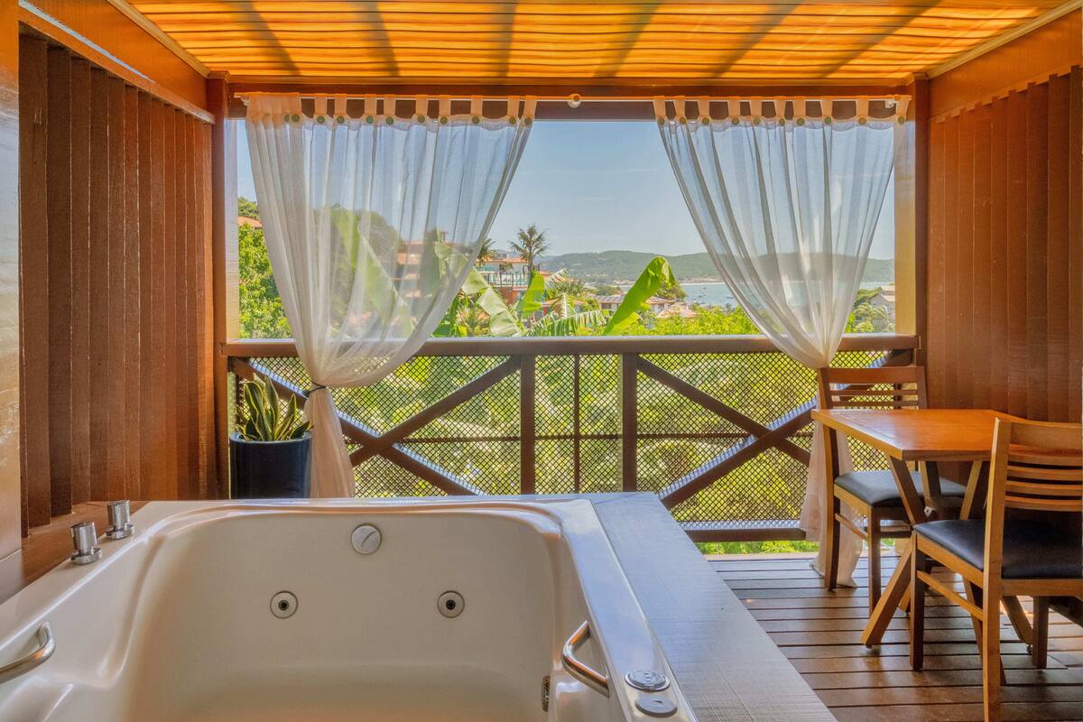 A balcony with a view of a coastal landscape, a wooden deck, and a spa area with a bathtub.