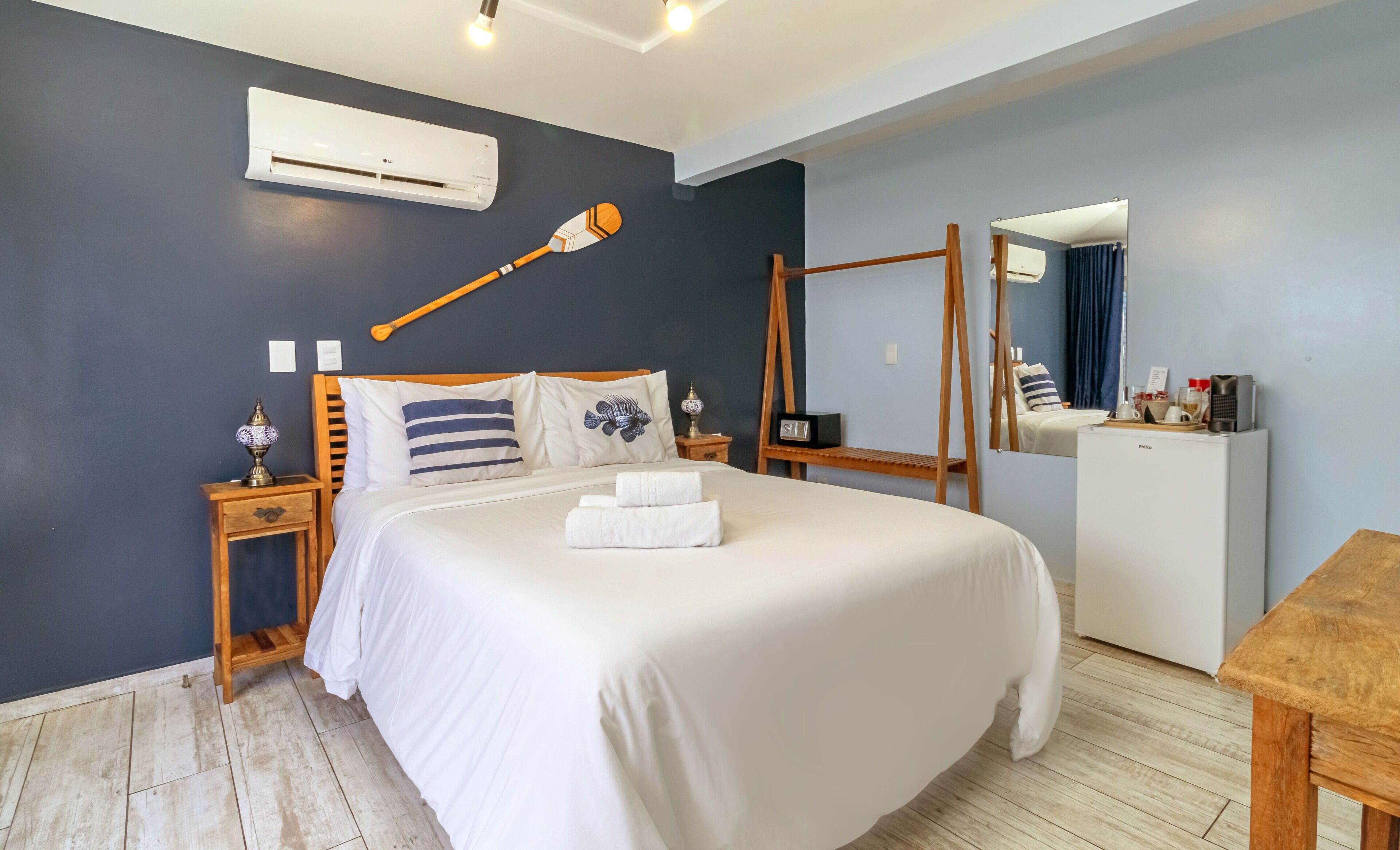 Une chambre à coucher comprenant un lit, des tables de chevet, un appareil de climatisation, un miroir, un banc en bois et un bureau avec une chaise.