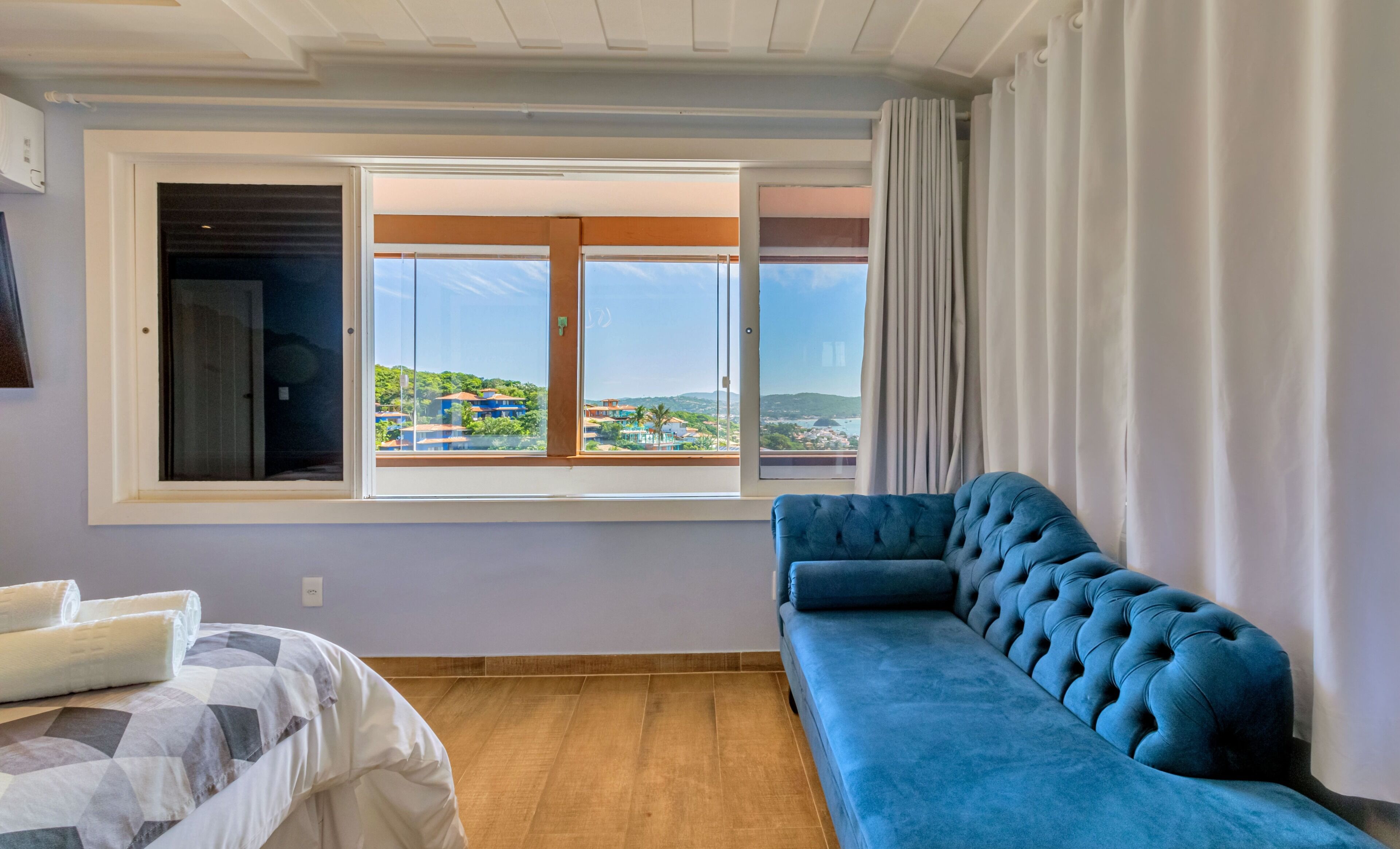 Una habitación con un ventanal grande, un sofá azul y una cama con colcha estampada.