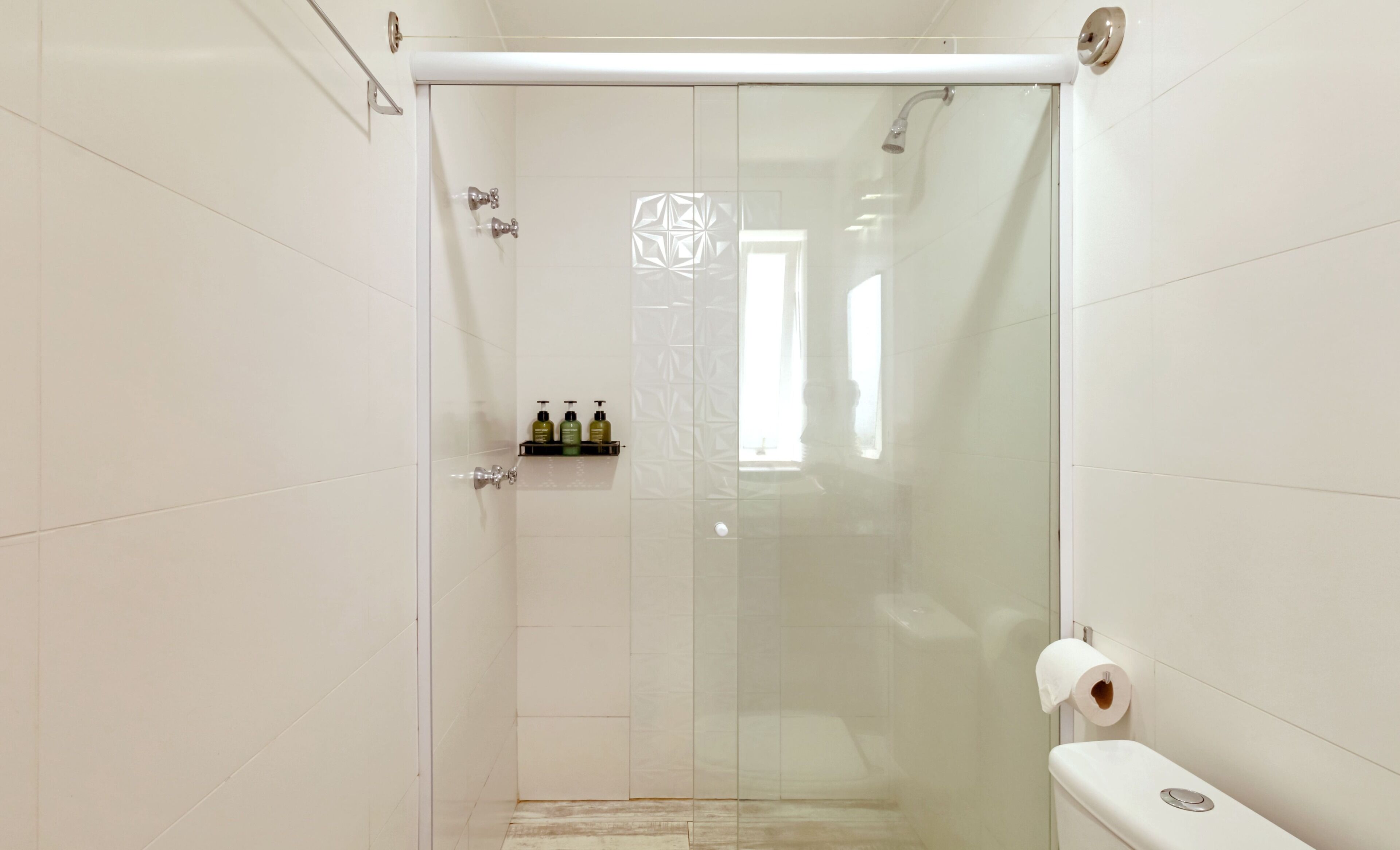 A modern bathroom with a glass shower enclosure, a toilet, and a shelf with toiletries.
