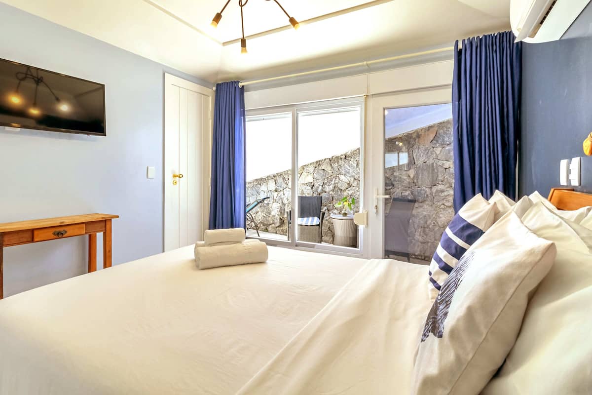 A bedroom with a bed, a wooden table, a TV, and a view of the outdoors.