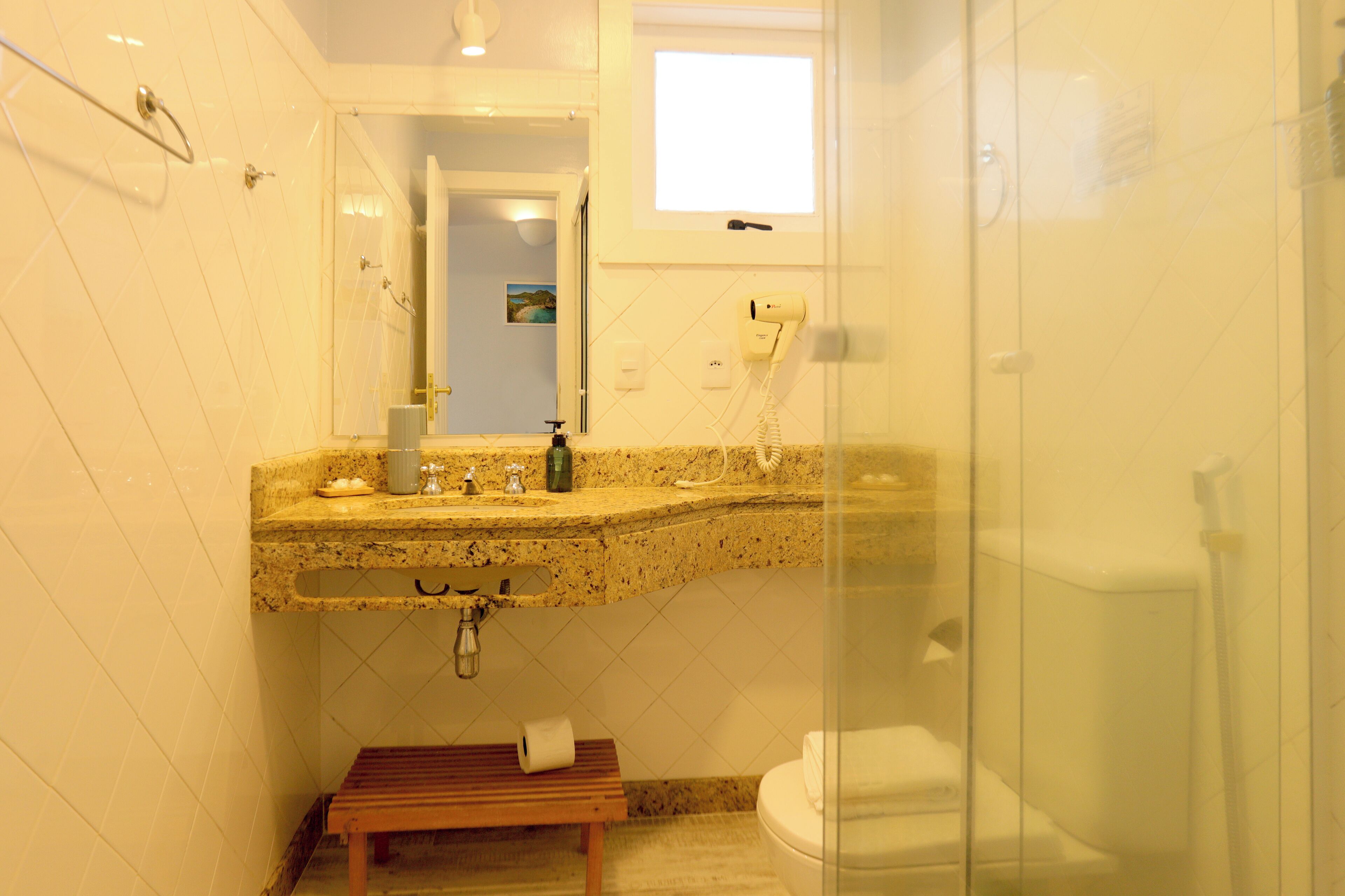 Un baño con encimera de granito, un espejo, toallero, inodoro y un banco.