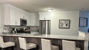 A modern kitchen with white cabinets, stainless steel appliances, and a bar area with three bar stools. - Okemo Ski in-Ski out @ Winterplace, 3 bdr, 2 ba Condo with Pool, Hot Tub, W/D (Ludlow)