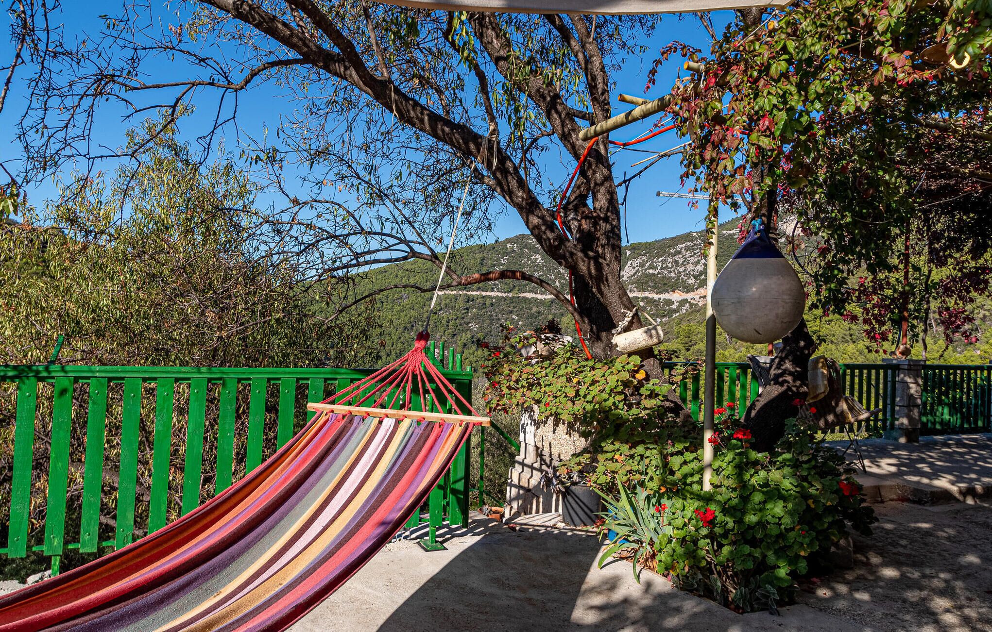 A hammock, a green fence, and a stone wall with a potted plant.