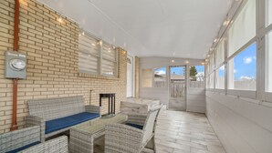 Een overdekt terras met rieten meubilair, een bakstenen muur en grote ramen.