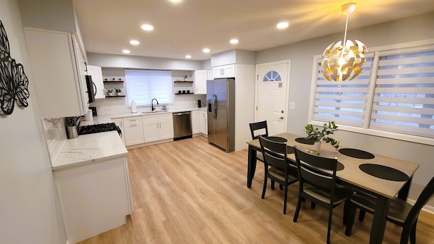 Een moderne keuken met witte kasten, een roestvrijstalen koelkast en een eethoek met een houten tafel en stoelen.