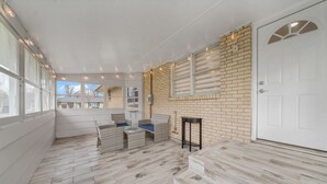 Een overdekt buitengebied met rieten meubels, een bakstenen muur en een witte deur.