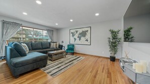 Een moderne woonkamer met een grijze modulaire bank, een klein armstoel in teal, een houten salontafel en een wereldkaart aan de muur.