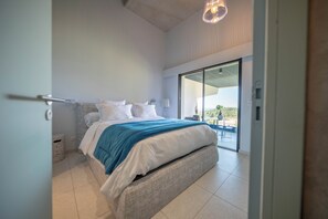 Quarto moderno com uma cama grande, vista através de uma porta de correr de vidro e uma luminária no teto.