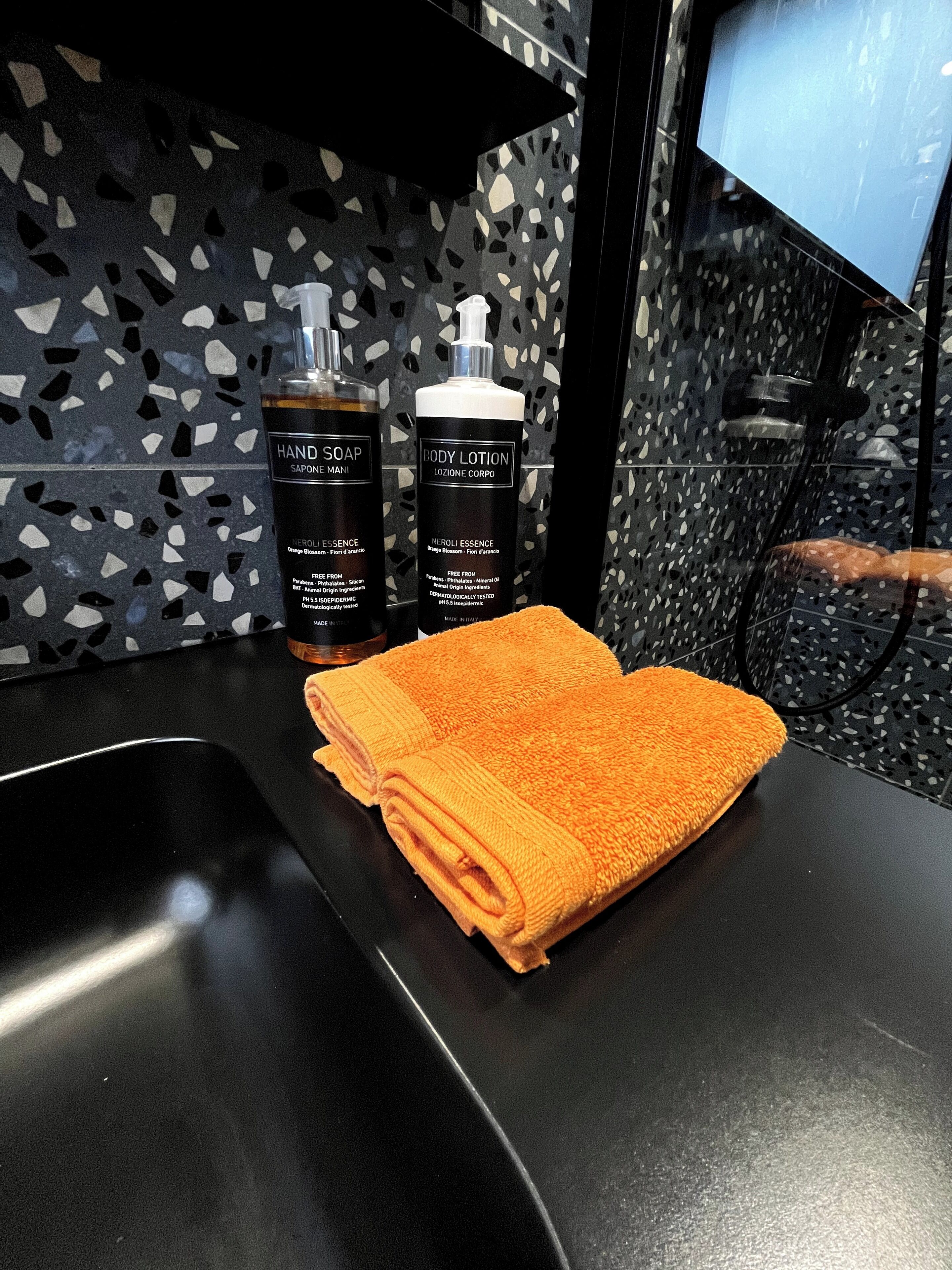 A bathroom with a black countertop, two bottles of hand soap and body lotion, and a folded orange towel.