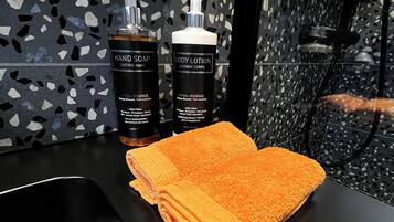 A bathroom with a black countertop, two bottles of hand soap and body lotion, and a folded orange towel.